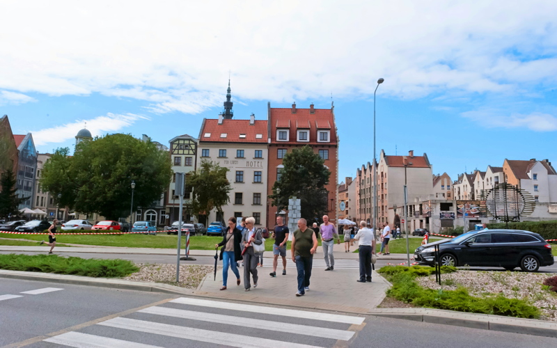 9 - Street view in the city center of Elbląg, Poland, featuring pedestrians crossing a street near historic architecture, including the Hotel Pod Lwem visible in the background
